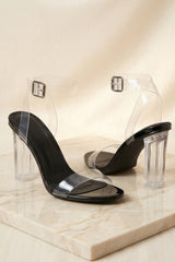 Femme Luxe black barely there sandals with clear ankle straps, open toes, and transparent block heels displayed on a marble pedestal