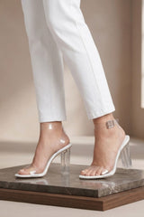 Femme Luxe white strappy clear block heel sandals with perspex straps, worn with white trousers for an elegant barely there look