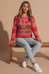 Model wearing a pink and red striped festive jumper with glitter Eat Drink Merry lettering, light wash jeans and white trainers, seated on a wooden bench for Femme Luxe