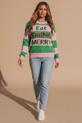 Model wearing a green and pink striped Christmas knitted jumper with glitter Eat Drink Merry lettering, light wash jeans and white trainers from Femme Luxe