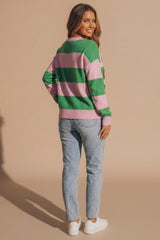 Femme Luxe model wearing a green and pink striped knitted jumper with light wash jeans and white trainers, shown from the back in a festive fashion setting